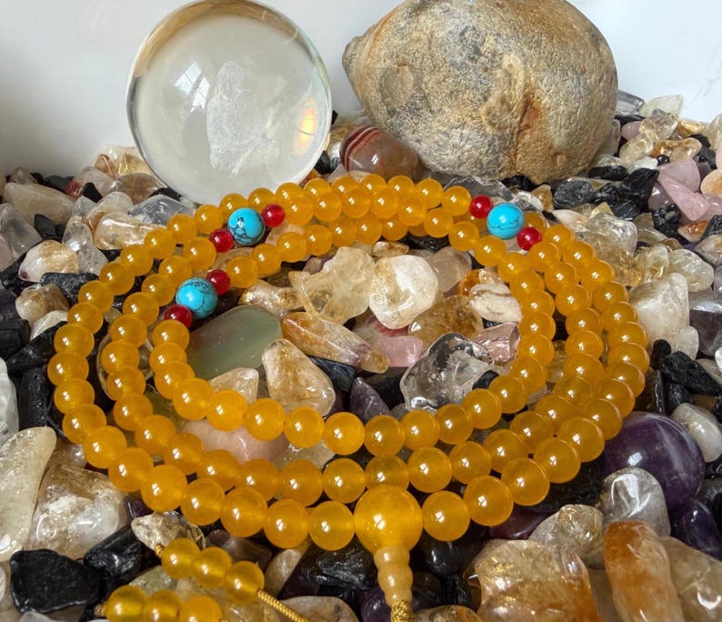 May include: A strand of yellow translucent beads arranged in a circular pattern, featuring interspersed bright turquoise round beads and small red accent beads. A larger yellow bead serves as a focal point at the bottom of the circular arrangement.