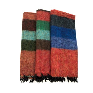 May include: Three folded, striped scarves in shades of red, brown, green, blue, and black. Each scarf has a different color scheme, with fringed edges. The scarves are made of a textured material.