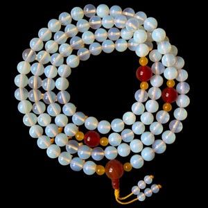May include: A long strand of translucent, milky white opalite beads arranged in a circular pattern. The necklace features several larger, smooth, deep red spherical beads and smaller, vibrant yellow accent beads, ending in a tassel with yellow cord.