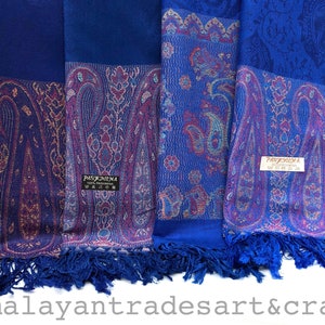 May include: Four blue Pashmina scarves with detailed paisley designs in purple, gold, and teal. Each scarf has a solid blue border and fringing. The scarves are labelled with a tag that reads "PASHMINA".