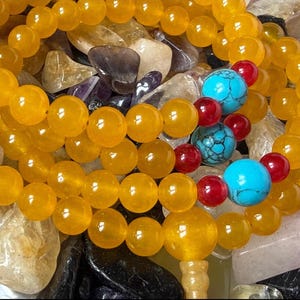 May include: A beaded bracelet or necklace featuring smooth, round, translucent yellow beads. The strand is accented with three larger, round, bright turquoise beads with dark veining, interspersed with smaller, round, glossy red beads.