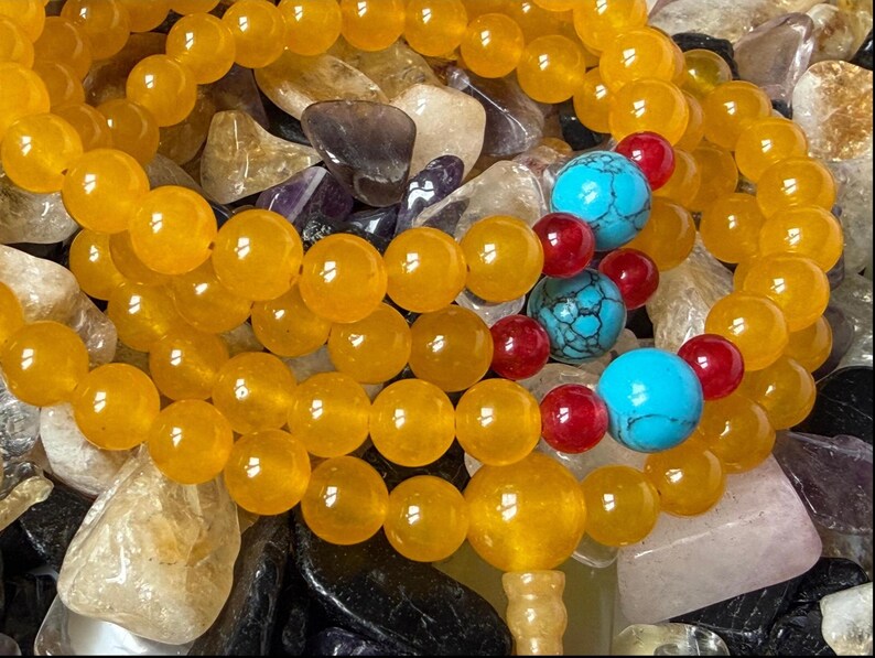 May include: A beaded bracelet or necklace featuring smooth, round, translucent yellow beads. The strand is accented with three larger, round, bright turquoise beads with dark veining, interspersed with smaller, round, glossy red beads.