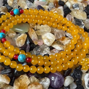 May include: A strand of prayer beads featuring smooth, round, translucent yellow beads. The strand is accented with three larger, round, blue turquoise-colored beads with dark veining, each flanked by two small, round, translucent red beads.
