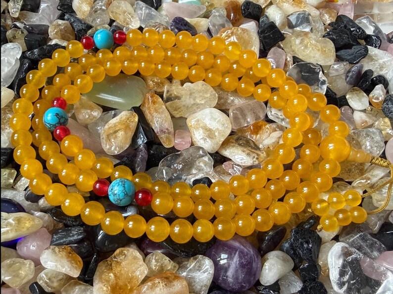May include: A strand of prayer beads featuring smooth, round, translucent yellow beads. The strand is accented with three larger, round, blue turquoise-colored beads with dark veining, each flanked by two small, round, translucent red beads.