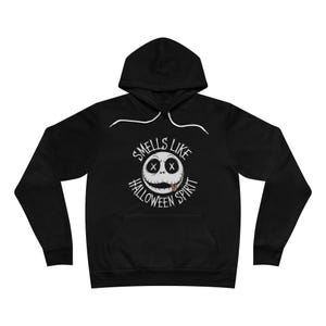 May include: Black hooded sweatshirt with a white graphic of a round face with stitched eyes and a stitched mouth with a tongue sticking out. The text "SMELLS LIKE HALLOWEEN SPIRIT" is above and below the face.