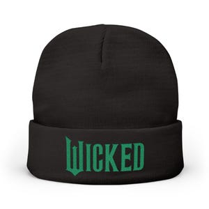以下が含まれることがあります： 前面に緑色の「WICKED」の文字が刺繍された黒いビーニー帽。帽子は無地で、折り返しのカフが付いています。テキストは様式化されたフォントです。