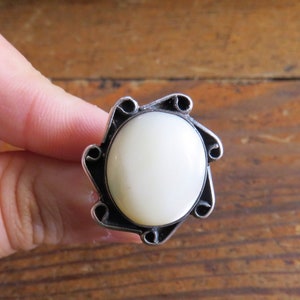May include: A silver ring with a white, round gemstone set in a decorative, swirling design.