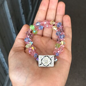 May include: A multi-colored crystal bracelet with a silver clasp. The bracelet is made of pink, blue, green, and clear crystals.
