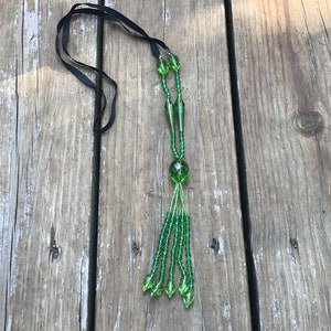 Op de afbeelding: Een groene glazen kralenketting met een kwast. De ketting heeft een zwarte strik.