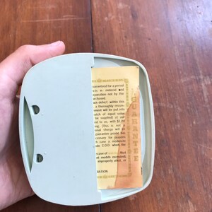 May include: A close-up of a small, light green plastic box with a yellow warranty card inside. The card has text that reads "GUARANTEE" and details a warranty for a period of time for defects in material and workmanship.