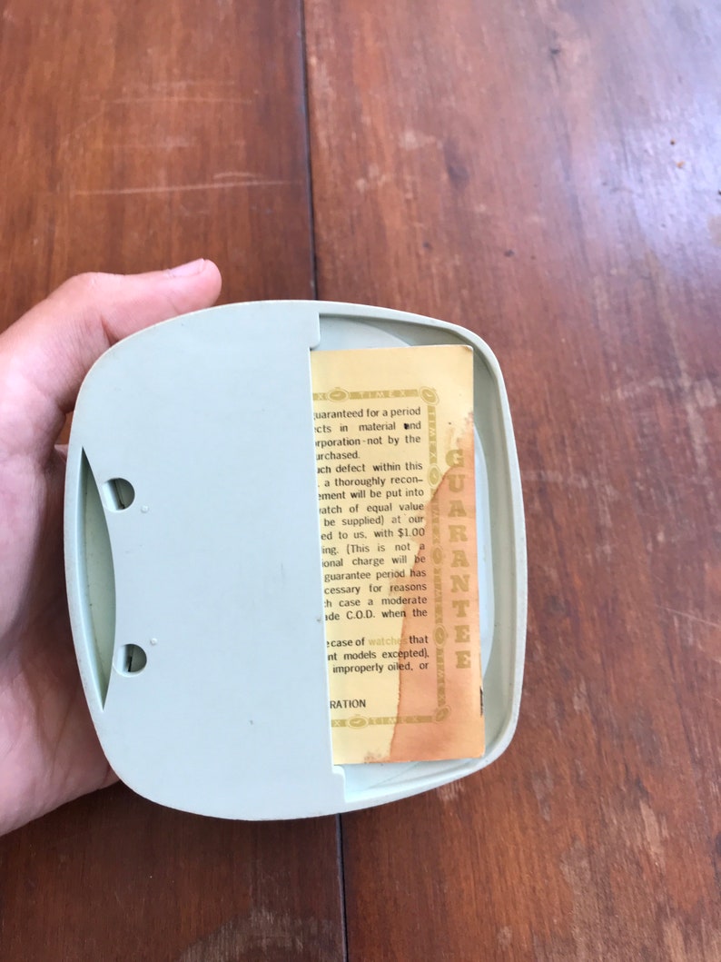 May include: A close-up of a small, light green plastic box with a yellow warranty card inside. The card has text that reads "GUARANTEE" and details a warranty for a period of time for defects in material and workmanship.