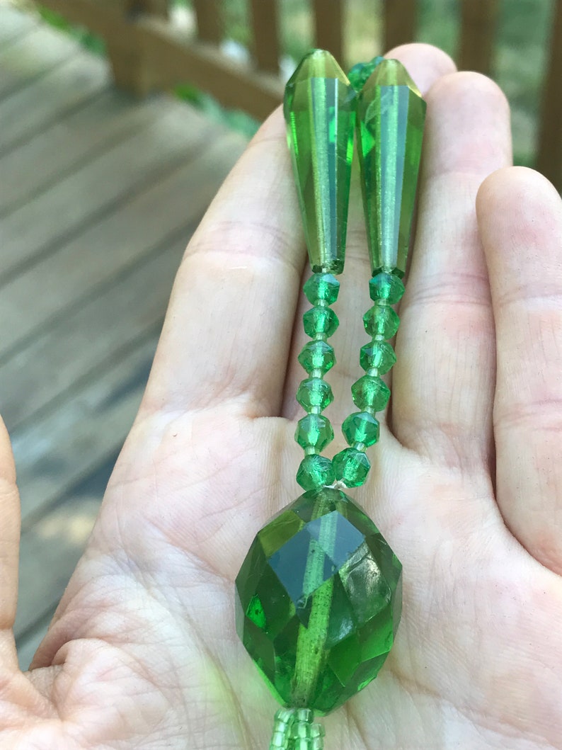 Op de afbeelding: Een groene glazen kralenketting met een grote gefacetteerde hanger en twee traanvormige kralen aan de bovenkant.