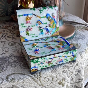 May include: A rectangular, hinged box with a detailed, colorful, raised relief design. The box features a lid and sides decorated with figures in a landscape. The color palette includes white, blue, green, yellow, and red.