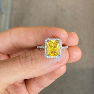 May include: A yellow gemstone ring with a square halo setting. The ring is set in silver and has a band of small diamonds.