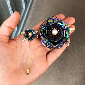 Peut inclure: Deux broches en forme de fleurs iris&eacute;es avec des accents dor&eacute;s et des centres de perles. La plus grande broche est une fleur plus grande avec plus de p&eacute;tales. La plus petite broche est une fleur plus petite avec moins de p&eacute;tales.