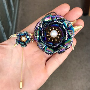 Peut inclure: Deux broches en forme de fleurs iris&eacute;es avec des accents dor&eacute;s. La plus grande broche a une perle au centre. Les deux broches ont un fermoir &agrave; &eacute;pingle.