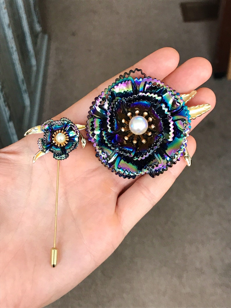 Peut inclure: Deux broches en forme de fleurs iris&eacute;es avec des accents dor&eacute;s. La plus grande broche a une perle au centre. Les deux broches ont un fermoir &agrave; &eacute;pingle.