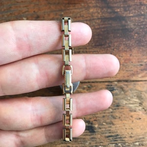 May include: A gold-toned watch band with a box-style chain link design.