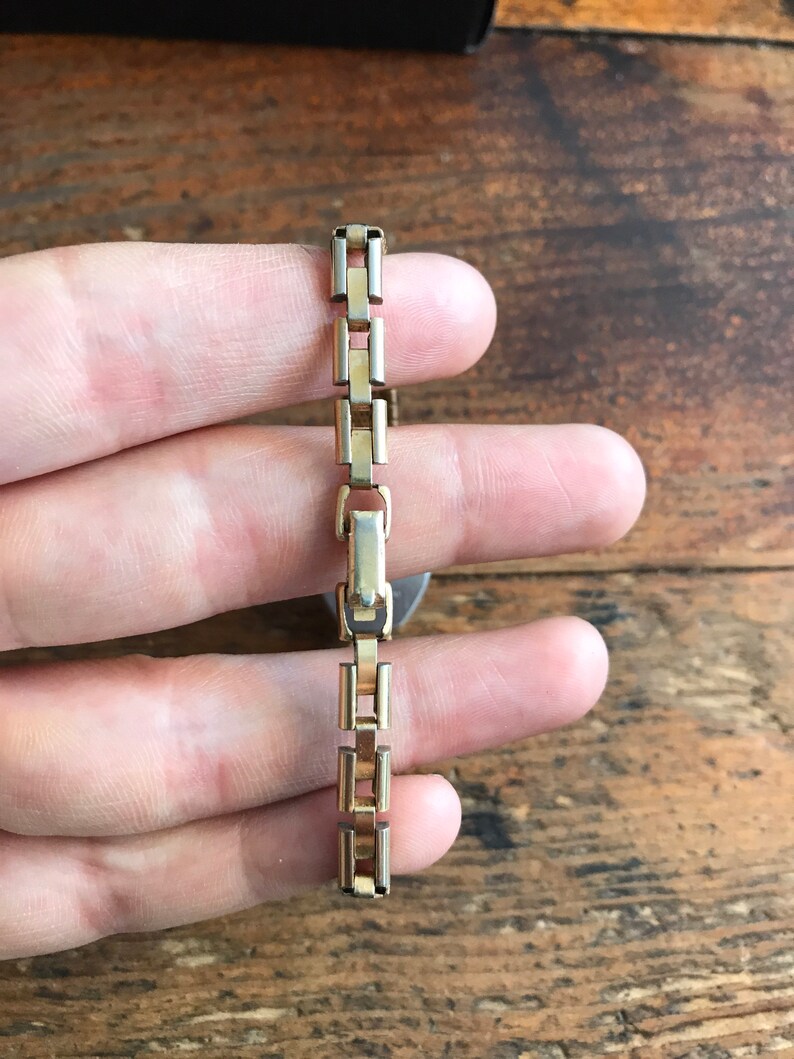 May include: A gold-toned watch band with a box-style chain link design.