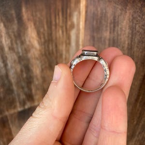 May include: A silver ring with a textured band and a rectangular black stone set in the top.