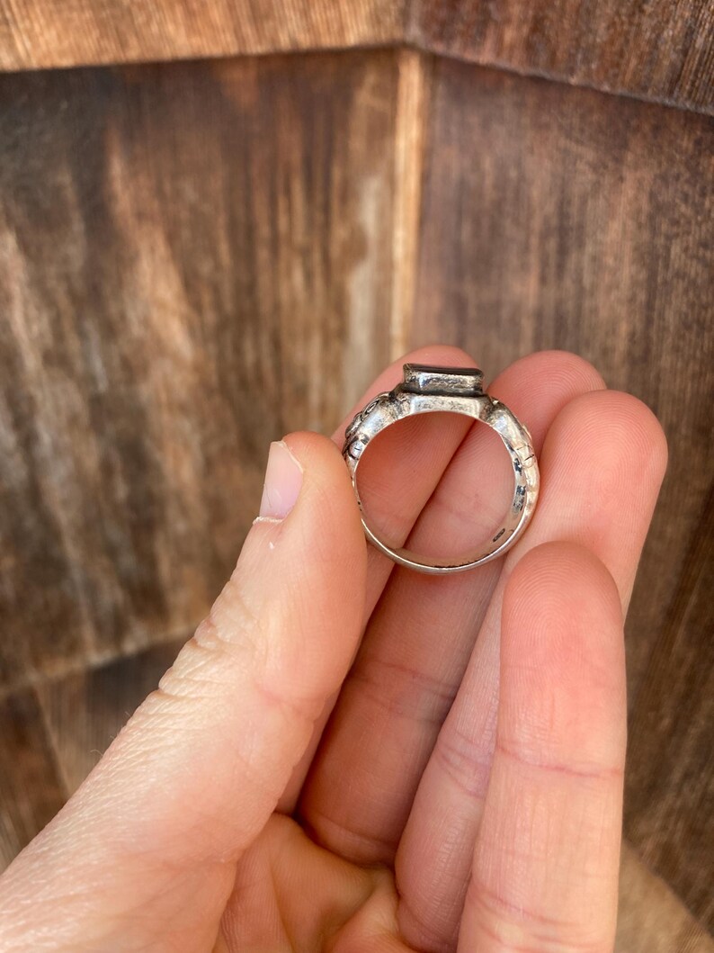 May include: A silver ring with a textured band and a rectangular black stone set in the top.