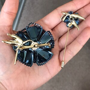 Peut inclure: Deux broches dor&eacute;es en forme de fleurs. La plus grande broche est une fleur noire avec des accents dor&eacute;s. La plus petite broche est une fleur dor&eacute;e avec des accents noirs.