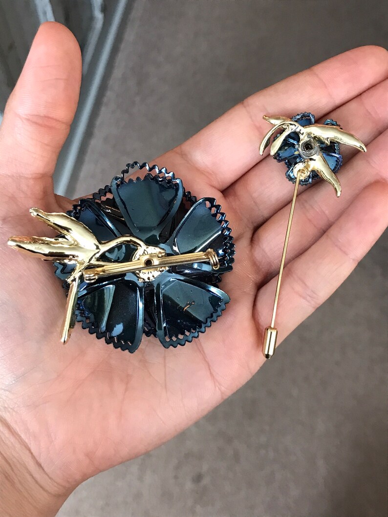 Peut inclure: Deux broches dor&eacute;es en forme de fleurs. La plus grande broche est une fleur noire avec des accents dor&eacute;s. La plus petite broche est une fleur dor&eacute;e avec des accents noirs.