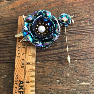 Peut inclure: Une broche en forme de fleur bleu iris&eacute; et or avec un centre en perle. La broche est fix&eacute;e &agrave; une &eacute;pingle en or.