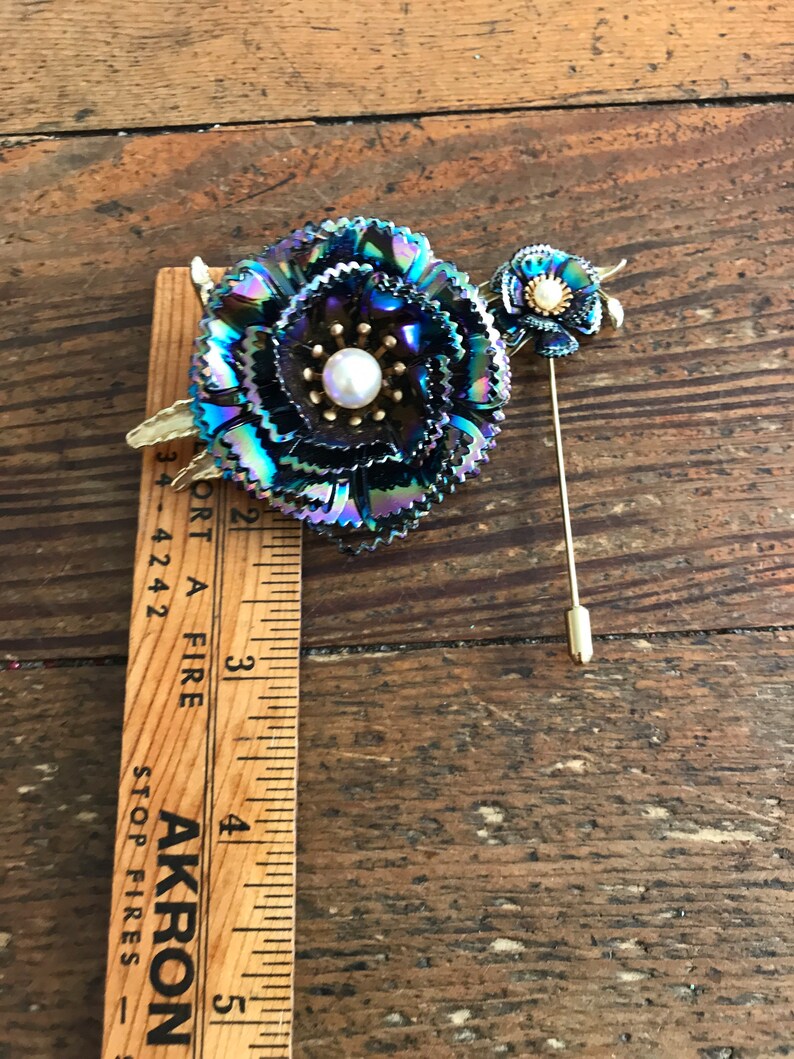 Peut inclure: Une broche en forme de fleur bleu iris&eacute; et or avec un centre en perle. La broche est fix&eacute;e &agrave; une &eacute;pingle en or.