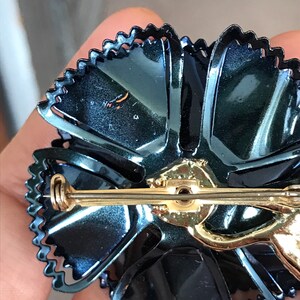 Peut inclure: Une broche en forme de fleur en &eacute;mail bleu fonc&eacute; avec une &eacute;pingle dor&eacute;e et un bord festonn&eacute;.