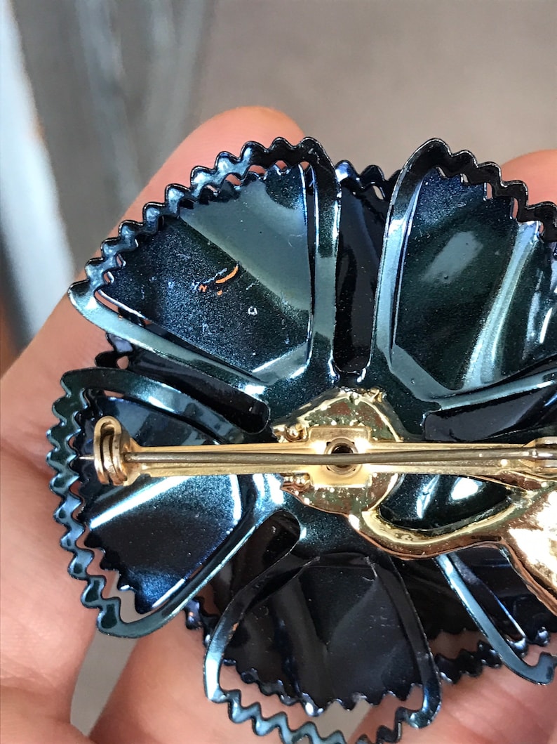 Peut inclure: Une broche en forme de fleur en &eacute;mail bleu fonc&eacute; avec une &eacute;pingle dor&eacute;e et un bord festonn&eacute;.