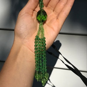 Op de afbeelding: Een groene glazen kralenkwast met een grote, gefacetteerde, groene glazen hanger.