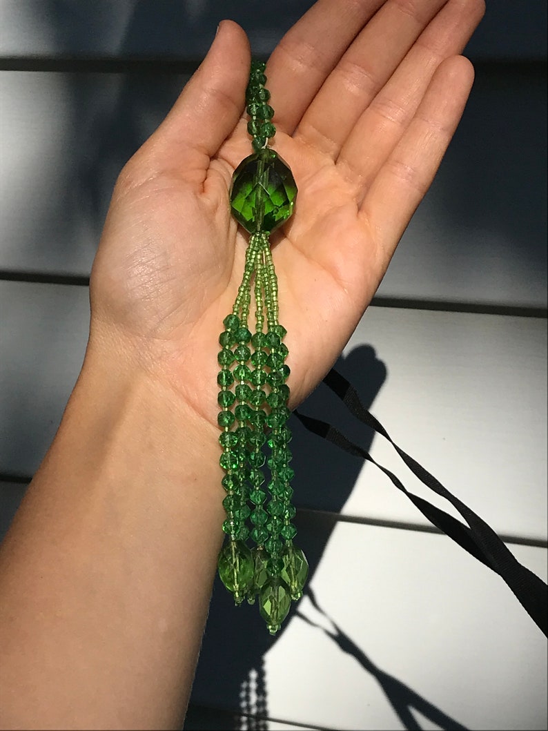 Op de afbeelding: Een groene glazen kralenkwast met een grote, gefacetteerde, groene glazen hanger.