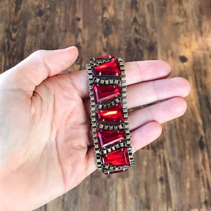 May include: A red and gold bracelet with large, faceted red stones set in a gold chain link design.