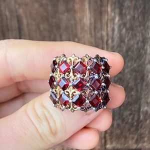 May include: A silver and gold ring with a band of red gemstones set in a filigree design.