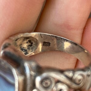 May include: Silver ring featuring a blue and white abalone shell inlay and intricate silver detailing. The ring is marked "925" on the inside band.