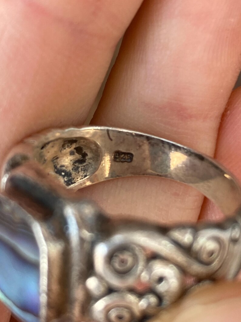May include: Silver ring featuring a blue and white abalone shell inlay and intricate silver detailing. The ring is marked "925" on the inside band.