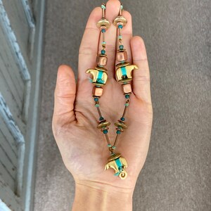 May include: A long necklace with copper and gold beads, featuring two small bear charms with turquoise accents.