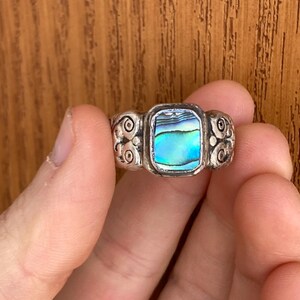 May include: A silver ring featuring a rectangular abalone shell inlay. The ring band has a decorative design.