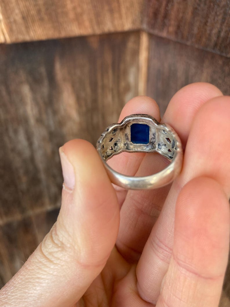 May include: A silver ring with a blue stone set in the centre. The ring has a detailed design around the stone.