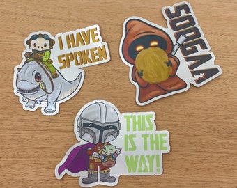 May include: Three Star Wars themed stickers. The first sticker features a cartoon of a character riding a creature with the text "I Have Spoken". The second sticker features a cartoon of a character with the text "Sooga". The third sticker features a cartoon of a character holding a baby with the text "This is the Way!"