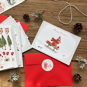 May include: A set of Christmas cards with a red envelope and a sticker featuring a fox and a rabbit on a sled. The card features a fox on a sled with the text "Merry Christmas".