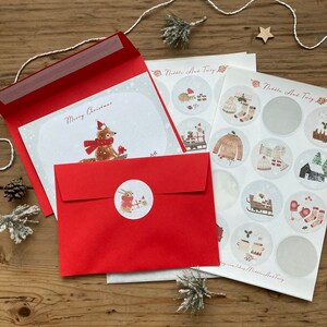 May include: A red envelope with a white card inside. The card has a drawing of a fox wearing a red hat and scarf. The text "Merry Christmas" is written on the card. The envelope has a sticker of a rabbit wearing a red hat and scarf. The image also shows a sheet of stickers with various winter-themed designs.