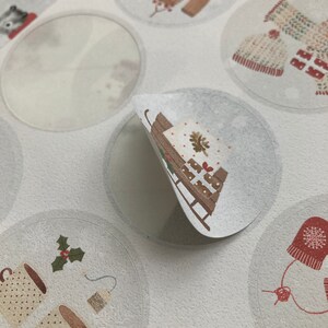 May include: A sheet of round, white stickers with various winter-themed illustrations. The stickers feature images of a sled with a wrapped gift, a mug of hot cocoa with holly, a sweater, a knitted hat, and a blank sticker.