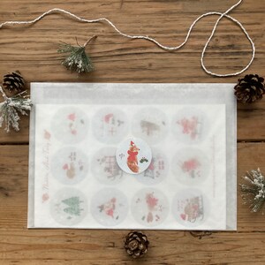 May include: A white envelope with a sheet of paper inside. The paper has 12 round stickers with various Christmas-themed illustrations. The stickers feature a fox, a Christmas tree, a house, and other wintery designs. The text "Merry little Tiny Fox" is printed on the paper.