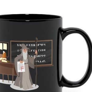 May include: Black ceramic mug with a white illustration of a wizard holding a failing grade in front of a chalkboard with runes. The text on the chalkboard reads "FANN", "LYK", "LAMPRT", and "PNADL".