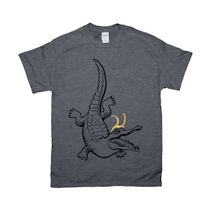 May include: A dark heather grey t-shirt with a black and white illustration of an alligator wearing a gold crown.