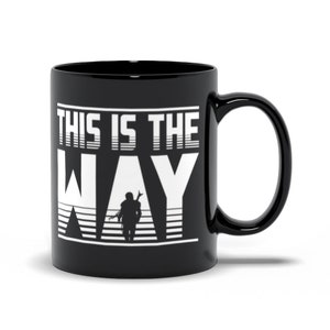 Puede incluir: Taza de caf&eacute; de cer&aacute;mica negra con un gr&aacute;fico blanco de una figura subiendo escaleras con el texto "This is the Way".