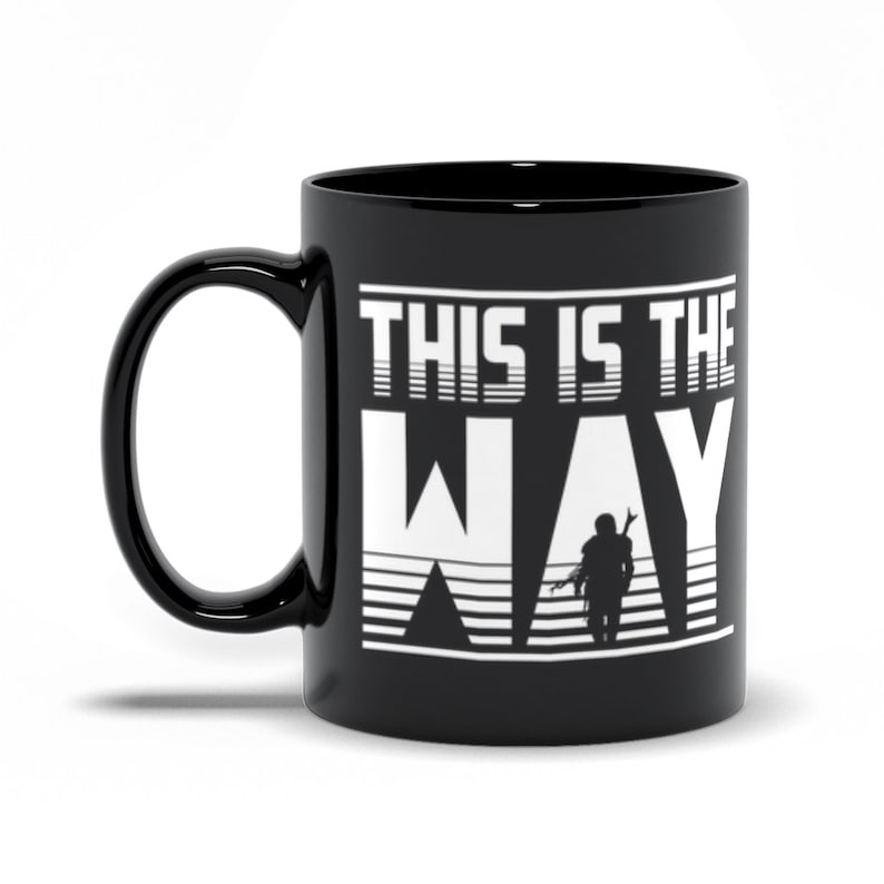 Puede incluir: Taza de caf&eacute; de cer&aacute;mica negra con un gr&aacute;fico blanco de una figura con una capucha y el texto "This is the Way".