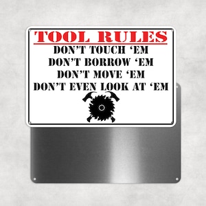 May include: White metal sign with black and red text that reads "TOOL RULES DON'T TOUCH 'EM DON'T BORROW 'EM DON'T MOVE 'EM DON'T EVEN LOOK AT 'EM". The sign has a black and white illustration of a saw blade with two hammers crossed behind it.